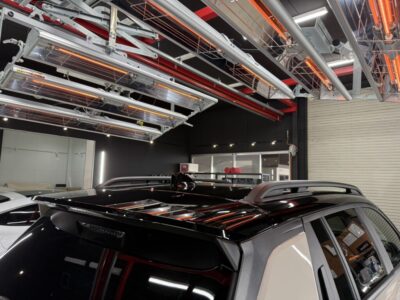 Black SUV inside a modern service bay with overhead industrial lighting and red/orange fixtures above.