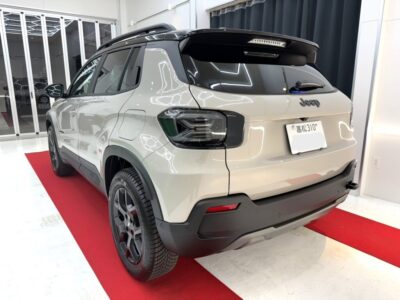 Rear view of a Jeep SUV on a red showroom carpet, indoors with glossy light-gray body and dark trim.
