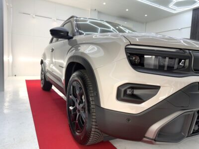 White SUV on a red showroom carpet, three-quarter front view highlighting the aggressive grille and block headlights.