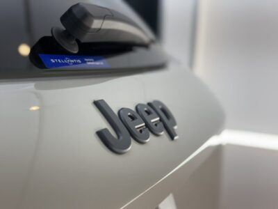 Close-up of a white Jeep rear with the black Jeep lettering and a blue Stellantis badge visible near the window accessory area.