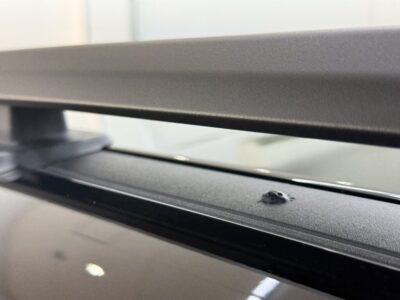 Close-up of a black car roof rail/track with a small circular plastic plug or screw head visible along the edge of the glass roof area.