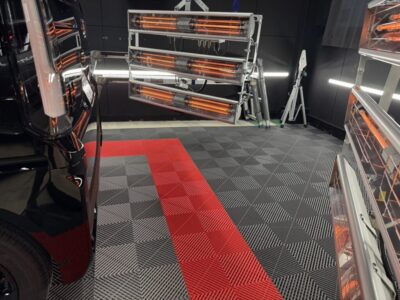 Workshop with multiple orange infrared heater panels on metal frames around a car service bay, red-and-black checkered floor.