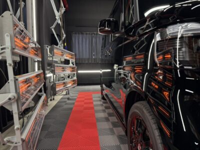 Black SUV in a high-tech workshop with infrared curing lamps along the left and a red runway on a checkered floor