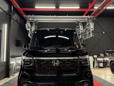 Front view of a shiny black Honda van parked inside a modern auto detailing shop with red steel beams overhead and bright ceiling lights.