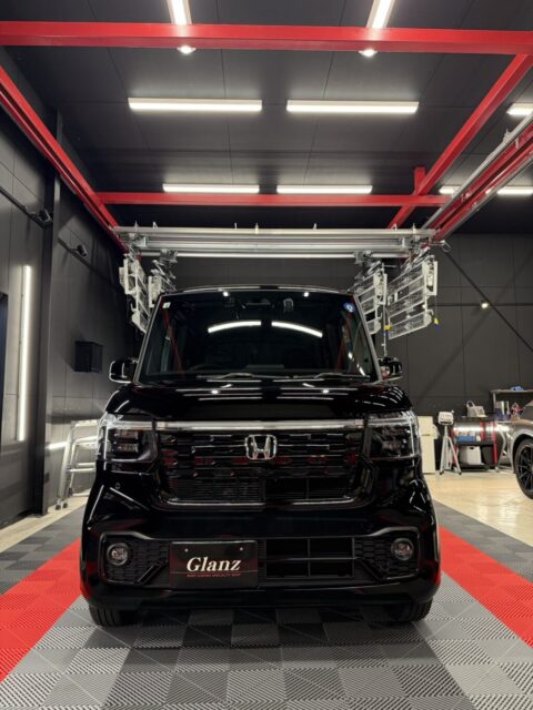 Front view of a shiny black Honda van parked inside a modern auto detailing shop with red steel beams overhead and bright ceiling lights.